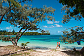 A woman and a man carrying a baby walk on an idyllic beach, Ile des Pins, New Caledonia, South Pacific