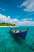 Ein buntes Boot treibt in klarem türkisfarbenen Wasser vor einer Insel, Senua, Indonesien
