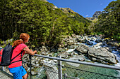 Woman looking from suspension bridge to Routeburn River, Routeburn Track, Great Walks, Fiordland National Park, UNESCO Welterbe Te Wahipounamu, Queenstown-Lake District, Otago, South island, New Zealand