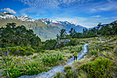Frau wandert auf Routeburn Track mit neuseeländischen Südalpen im Hintergrund, Routeburn Track, Great Walks, Fiordlands Nationalpark, UNESCO Welterbe Te Wahipounamu, Queenstown-Lake District, Otago, Südinsel, Neuseeland