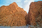 Cliffs of the Todra gorge with orange rocks,  small road passing the gorge, High Atlas, Morocco