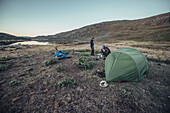 Hiker eating in front of a tent, greenland, arctic.