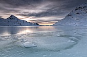 The smooth ice and choppy splits are enhanced by a dark sky clouded by fanciful glazes. White Lake. Bernina Pass. Canton of Graubuenden. Engadine. Switzerland. Europe.