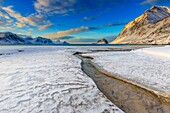 The golden sunrise reflected in a clear stream of the sea where the snow has melted. Haukland Lofoten Islands Norway Europe.