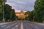 View over Maximiliansbruecke to Maximilianeum in the evening light with pedestrians and a guy taking pictures on the street, Munich, Upper Bavaria, Germany