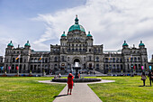 A Lady In Red Takes A Photo Of The British Columbia Parliament Buildings; Victoria, British Columbia, Canada