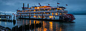 Lights illuminating a river boat docked on the Columbia River at dusk; Astoria, Oregon, United States of America