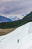 A woman ice climbs on Root Glacier in Wrangell-St. Elias National Park with Mt. Blackburn in the background; Alaska, United States of America