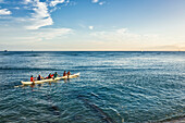 Tourists paddle in an outrigger canoe off Waikiki Beach; Waikiki, Oahu, Hawaii, United States of America