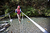 A Woman Walks On A Cable On A Suspension Bridge Over A River; Alaska, United States Of America
