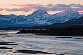 The sun sets on Mt. Deborah and Mt. Hess in the Alaska Range, viewed from the Susitna River bridge along the Denali Highway; Alaska, United States of America