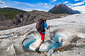 A backpacker crosses a stream on the surface of Root Glacier in Wrangell-St. Elias National Park. Donoho Peak is in the background; Alaska, United States of America