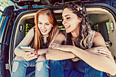 Two young women on a road trip sit in the back of a vehicle using a smart phone; Edmonton, Alberta, Canada