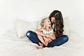 Portrait of a mother and young daughter sitting on a bed spending time together and laughing; Sorrento, British Columbia, Canada