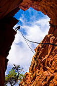 Looking upwards to the silhouette of an adventurer rappelling down a canyon in the desert; Hanksville, Utah, United States of America