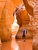 A female adventurer admiring the height of the slot canyon she is surrounded by water in; Hanksville, Utah, United States of America