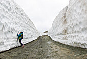 A woman hiking up a road on Whistler Blackcomb, on a gloomy spring day, were the snow has been cleared for the spring. Snow walls over 20 feet tall line both sides of the road. Whistler, British Columbia, Canada