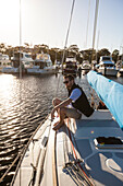 Sailor sitting on foredeck of sailboat, Perth, Western Australia, Australia