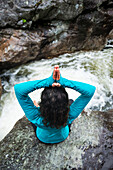 View from above of woman in lotus pose practicing yoga on rock in river, Gorham, New Hampshire, USA