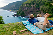Adult couple lying together on blanket and admiring ocean coastline, Bali, Indonesia