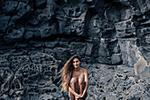 Woman in bikini sitting surrounded by volcanic rocks, Tenerife, Canary Islands, Spain