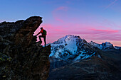 An hiker climbing a rock in Viola valley with a panoramic view at sunset. Valdidentro, Valtellina, Lombardy, Italy