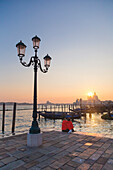 two tourists admire the sunset behind the domes of the Basilica of Saint Mary of Health from the banks of the Grand Canal, Venice, Veneto, Italy