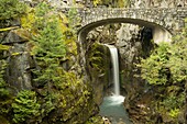 Christine Waterfall in Mt. Rainier National Park is framed by a stone bridge and rock cliffs.