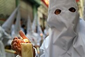 Nazarenos participating in a religious procession, with the traditional robes and hoods and carrying candles during Semana Santa (Easter) in Seville.