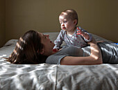 Smiling Woman and Baby Laying on Bed