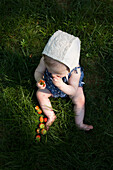 High Angle View of Young Baby Girl Sitting in Grass Eating Strawberries