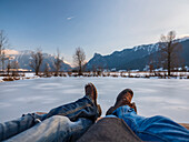 Two people enjoy the winter landscape on a frozen pond in the Ammergau Alps with a view of peak Kofl, Unterammergau, Upper Bavaria, Germany