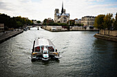 A sightseeing boat on the Seine River with the Notre Dame cathedral in the background.