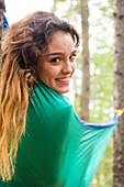 Smiling woman lying in hammock in forest and looking at camera