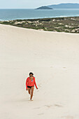 Young woman running in Joaquina sand dunes, Florianopolis, Santa Catarina, Brazil