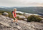 An active woman takes in in the view of the Atlantic Ocean from the summit of Pemetic Mountain while hiking in Maine's Acadia National Park.