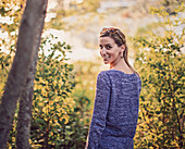 Portrait of young woman standing in forest and smiling while looking over shoulder, Maine, USA