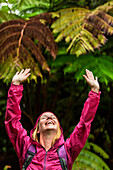A woman raises her arms in joy during a light rain shower while hiking a forest near Volcano National Park on the Big Island of Hawaii.