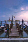 Gondolas tied up to wooden poles on the Canal Grande, in the background the monastery of San Giorgio Maggiore,Venice, Veneto, Italy