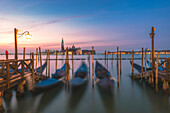 Gondolas tied up to wooden poles on the Canal Grande, in the background the monastery of San Giorgio Maggiore,Venice, Veneto, Italy