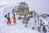 Zwei Personen auf Skitour blicken auf Geislergruppe, von der Puezspitze, Naturpark Puez-Geisler, UNESCO Weltnaturerbe Dolomiten, Dolomiten, Südtirol, Italien