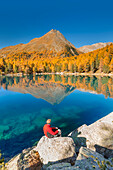 Hiker take a break to admire lake Saoseo in a perfect autumn day, Poschiavo, val di Campo, Canton of Graubunden, Switzerland, Europe