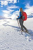 Young girl walks with snowshoes in the direction of the sun. Grevasalvas, Engadin Valley, Graubünden, Switzerland, Europe.