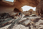 Man walking in desert with his mountain bike towards rock arch, Tenerife, Canary Islands, Spain