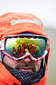 Members of an expedition cruise to Antarctica push off from Salisbury Plain on South Georgia in a Zodiak to head back to the expedition cruise ship, reflected in the goggles of an instructor.
