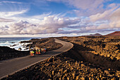 Group of cyclists pedaling on coastal road, Timanfaya National Park, Lanzarote, Canary Islands, Spain