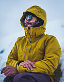 Smiling man in sunglasses and in yellow winter coat while climbing Mt Shasta, California, USA