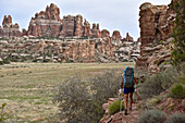 Female backpacker hiking in Canyonlands National Park with Needles rock formation in background, Moab, Utah, USA