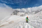 mountaineer climbing up a snow-covered slope emerging from the clouds in the heart of the massif of the mont-blanc, chamonix-mont-blanc, haute-savoie (74), france