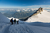 mountaineers roped together climbing down the snow-covered slope of the mont-blanc du tacul in the shade, the aiguille du midi and the chamonix valley lit up in the distance, massif of the mont-blanc, chamonix-mont-blanc, haute-savoie (74), france